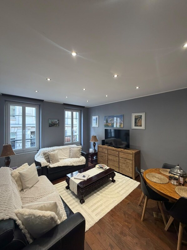 A modern living room with a sofa, a coffee table, a TV, and a dining area with chairs and a table.
