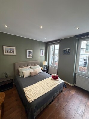 A bedroom with a large bed, a nightstand, a lamp, and a window.