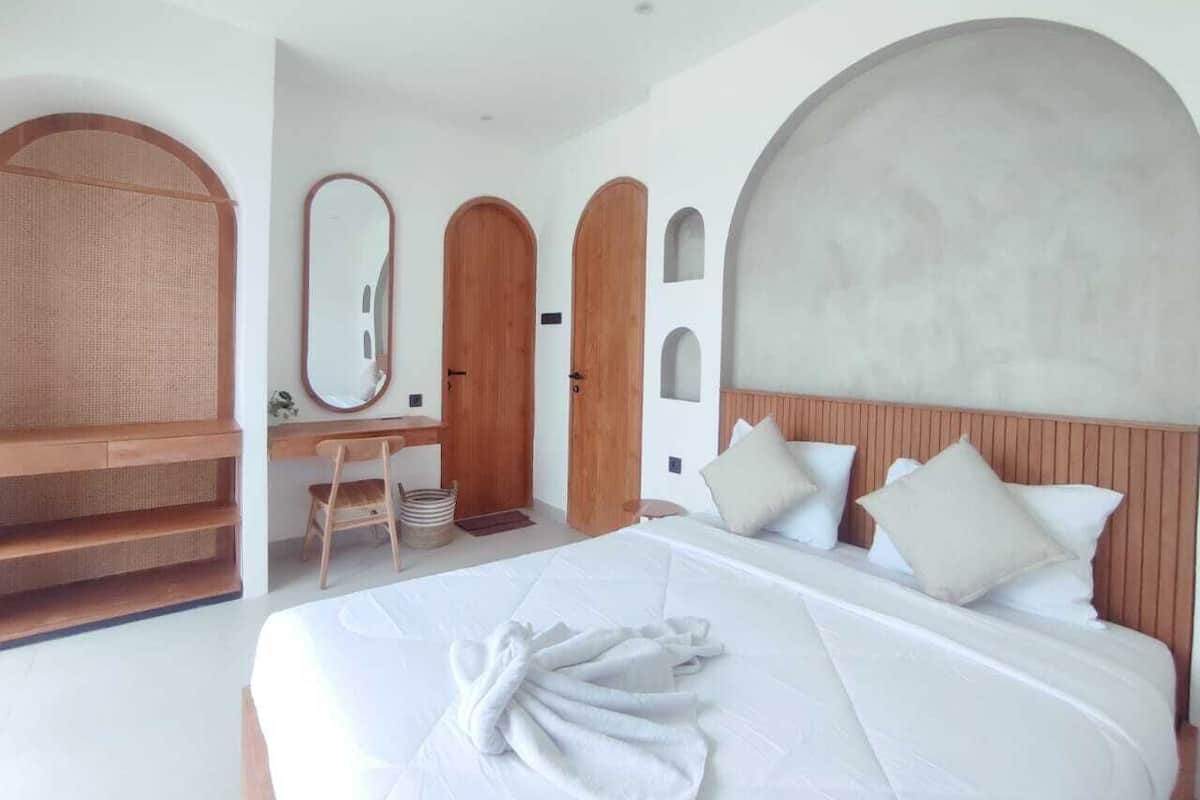 A modern hotel room with a large bed, wooden headboard, and a desk with a chair.