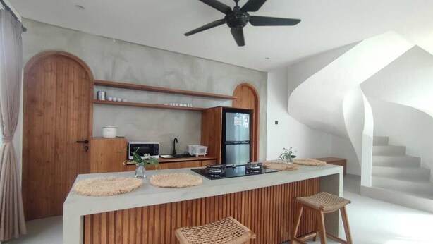 Une cuisine moderne dotée d’un îlot central, de tabourets de bar en bois, d’un ventilateur de plafond et d’un escalier menant à un niveau supérieur.