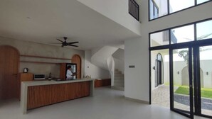 Un intérieur spacieux et moderne, avec un comptoir d’accueil central, un escalier et de grandes portes vitrées donnant sur l’extérieur.