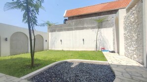 Une cour avec un chemin pavé de pierres, un petit arbre et un bâtiment doté d’un toit en tuiles.