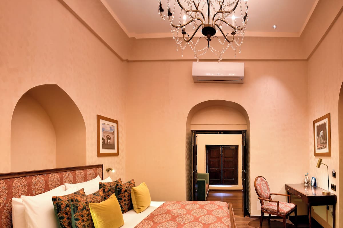 A hotel room with a large bed, a desk, and an arched doorway leading to another room.