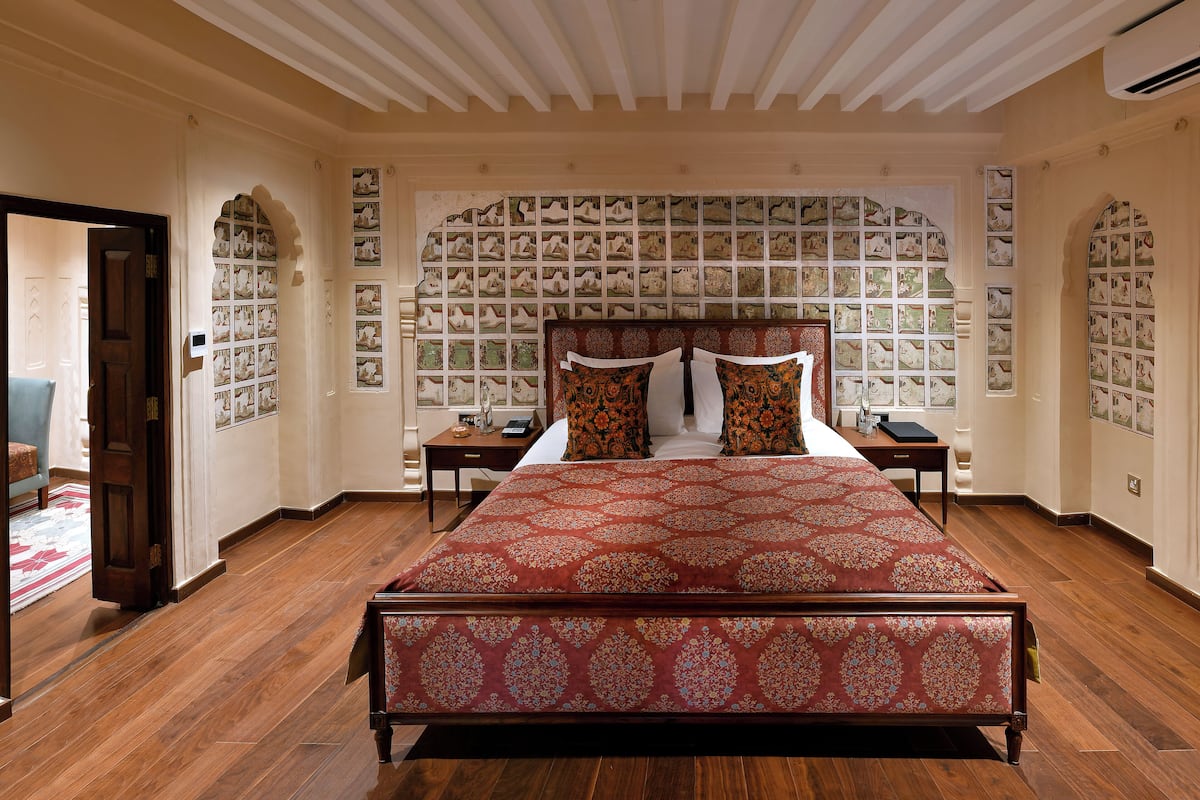 A spacious bedroom with a large bed, wooden floor, and a wall decorated with framed pictures.