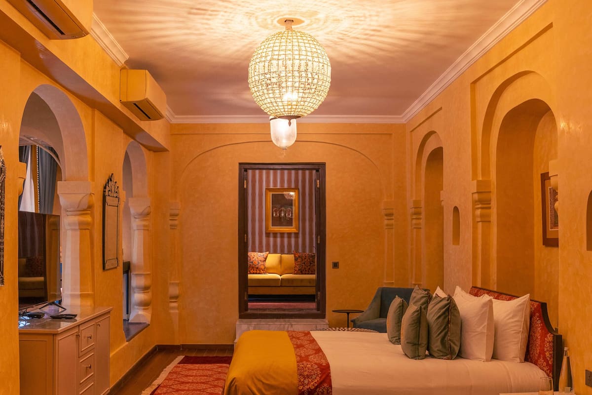 A hotel room with a large bed, a chandelier, and a view of the city through a window.