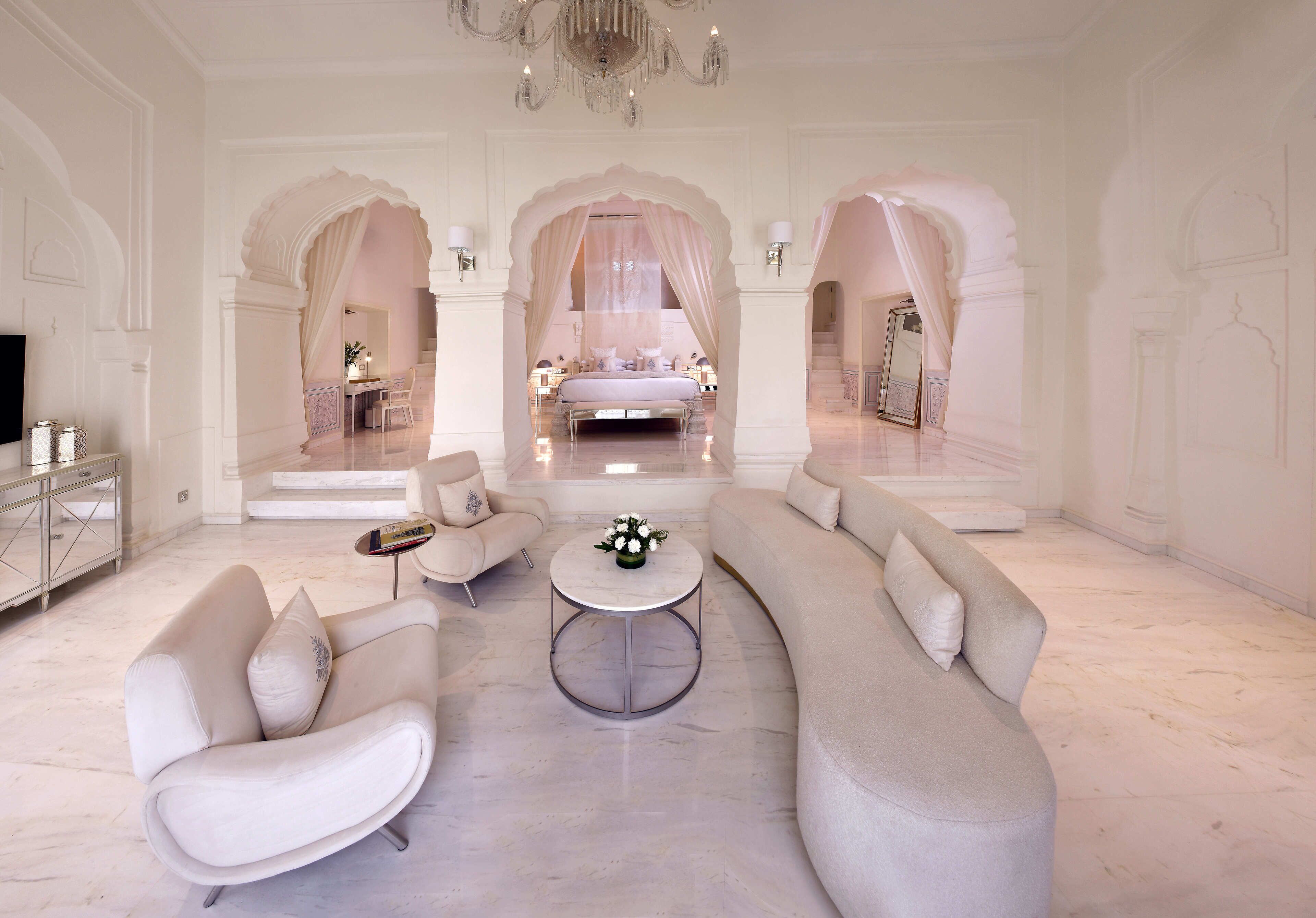 A luxurious living room with a large sofa, a coffee table, and a bed with a canopy in the background.
