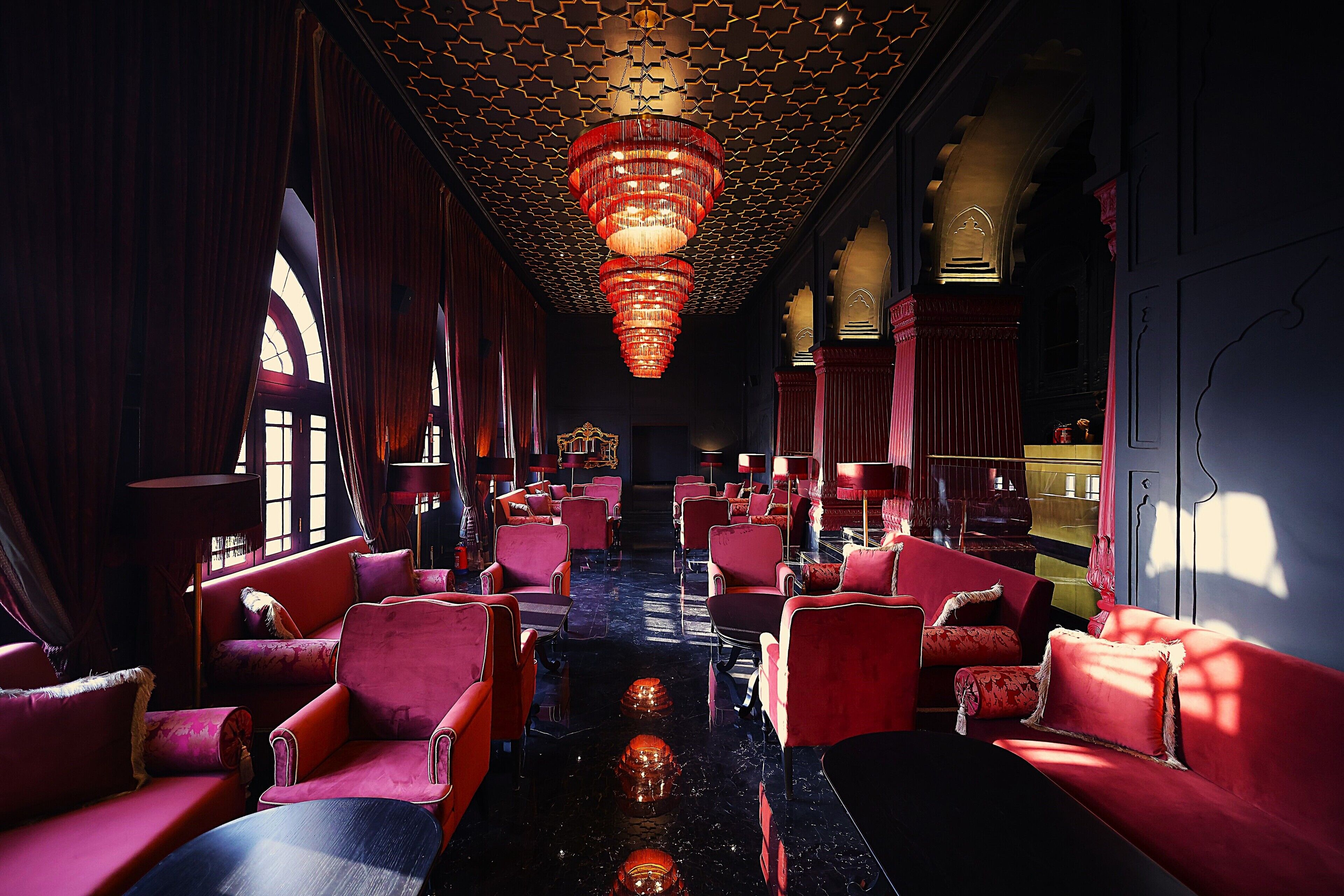 A luxurious interior with red upholstered seating, a reflective black floor, and a patterned ceiling.