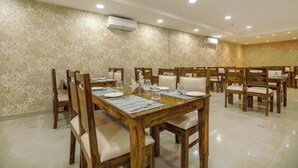 Zona pranzo con tavoli e sedie in legno, disposti in una stanza ampia con carta da parati decorata e illuminazione a soffitto incassata.