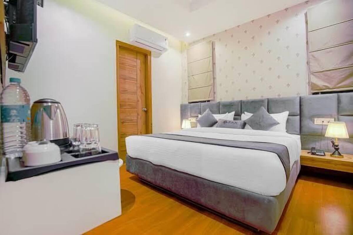 A hotel room with a bed, bedside table, lamp, and a wall-mounted air conditioner.