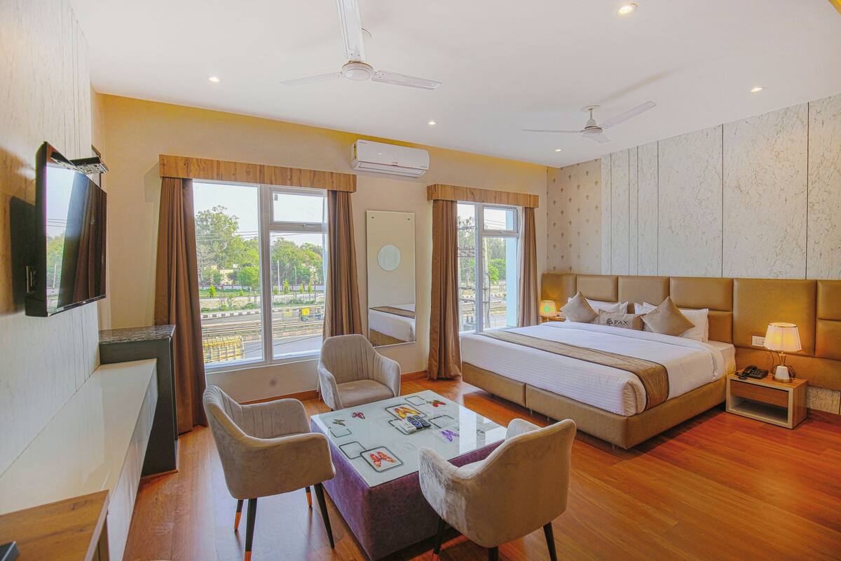 A hotel room with a large bed, two armchairs, a small table, a TV, and a window with curtains.