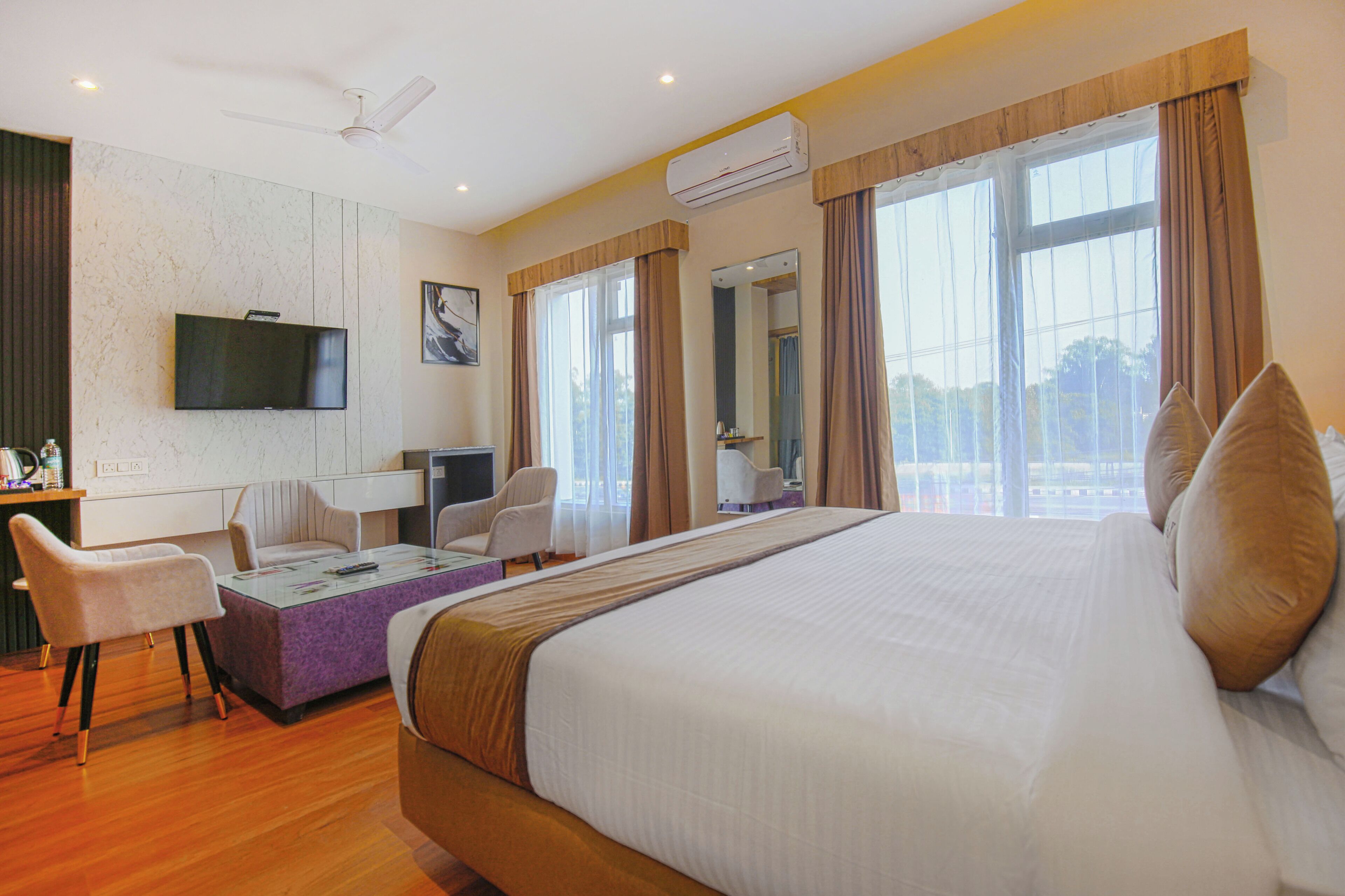 Quarto de hotel com uma cama grande, uma escrivaninha com cadeira, televisão e janela com cortinas.