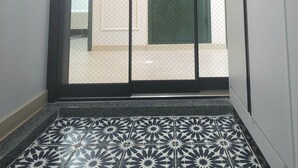Une pièce dotée d’un sol à motifs, d’une porte-fenêtre coulissante et donnant sur une autre pièce avec une porte et un luminaire.