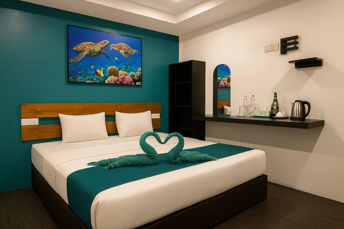 Une chambre d’hôtel avec un lit, un mur de couleur turquoise, un tableau représentant des tortues de mer, une serviette en forme de cœur, une étagère avec des articles de toilette et un miroir.