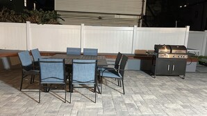 Un patio al aire libre con mesa, sillas y una parrilla.