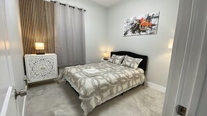 Un dormitorio con cama, mesita de noche, lámpara de pared y un cuadro.