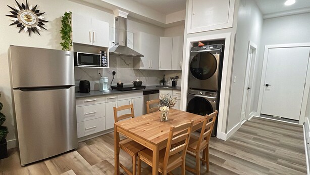 Cocina compacta con refrigerador, microondas, estufa y horno empotrado. Hay una mesa de comedor con sillas y un florero con flores.
