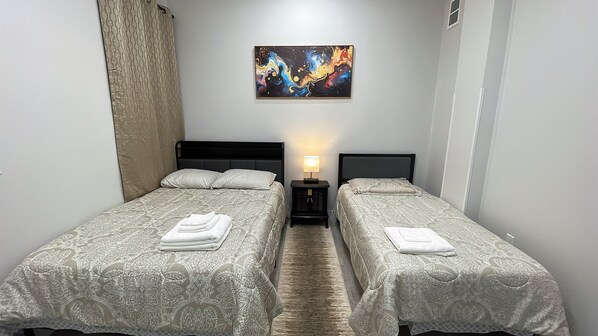 A hotel room with two beds, a nightstand with a lamp, and a colorful abstract painting on the wall.