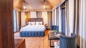 A bedroom with a large bed, a seating area with a table, and curtains on the windows. - The Whispering Oaks (Nainital)