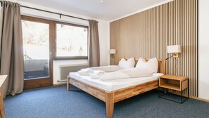 A bedroom with a wooden bed, a desk, a chair, a radiator, and a window with curtains. - Apartment near ski lift and ski bus in Brixen (Brixen)