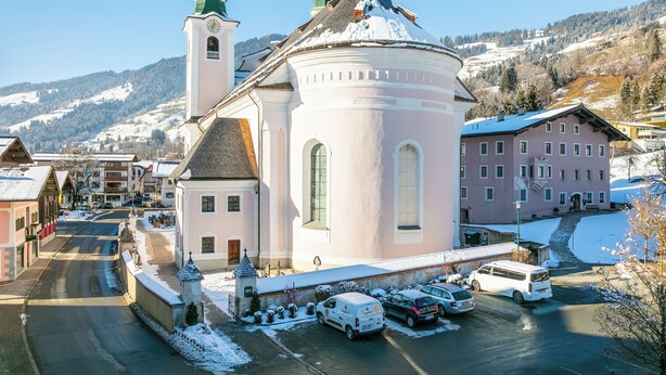 A historic church with a prominent bell tower and a round tower, surrounded by snow-covered buildings and a mountainous backdrop. - Apartment near ski lift and ski bus in Brixen (Brixen)