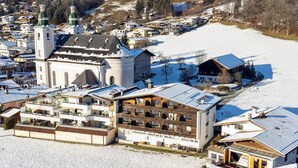 Une ville recouverte de neige, avec une église imposante, un immeuble à plusieurs étages doté de balcons et une maison en bois.