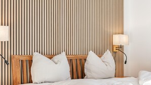 A neatly made bed with white bedding and pillows, a wooden headboard, and two bedside lamps.