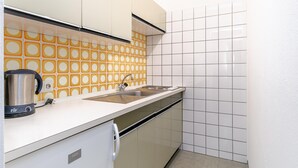 A compact kitchen with white cabinets, a sink, and a kettle on the counter.