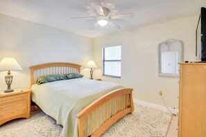 A bedroom with a bed, two bedside lamps, a ceiling fan, a window with blinds, and a dresser. - Walk to Coast: Condo in Daytona Beach Shores! (Daytona Beach Shores)