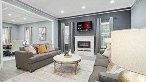 Una sala de estar moderna con chimenea, sofás grises, una mesa de centro y un televisor montado en la pared.