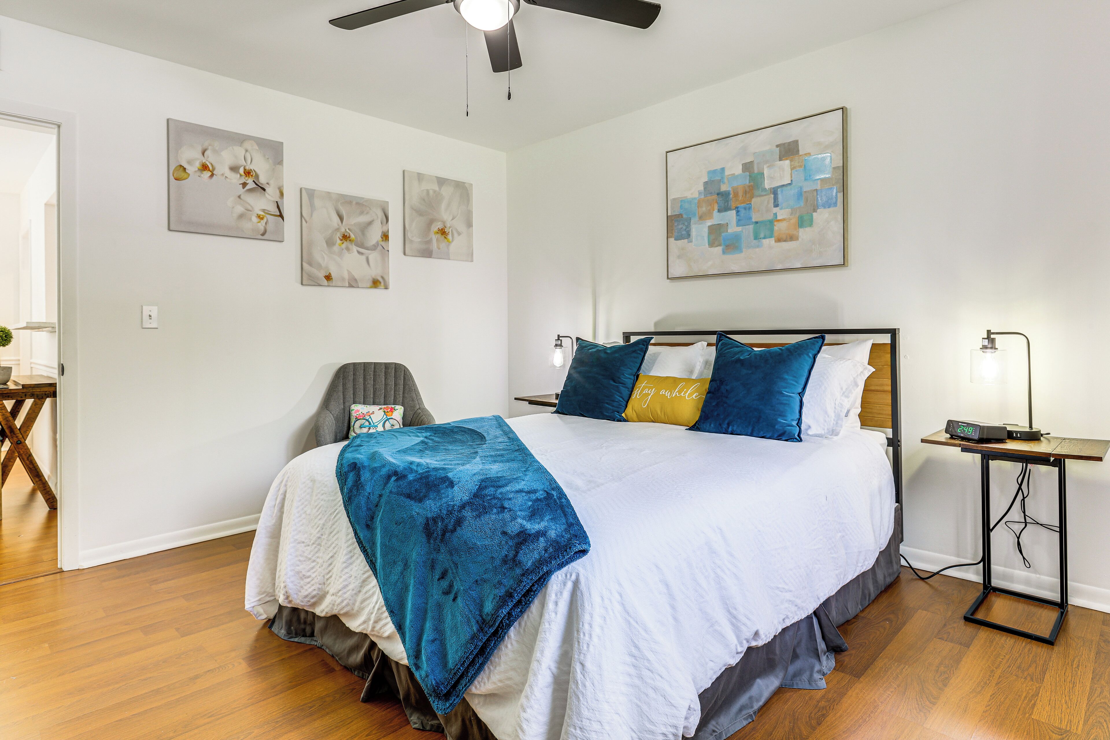 A bedroom with a bed, a bedside table, a chair, and artwork on the walls.