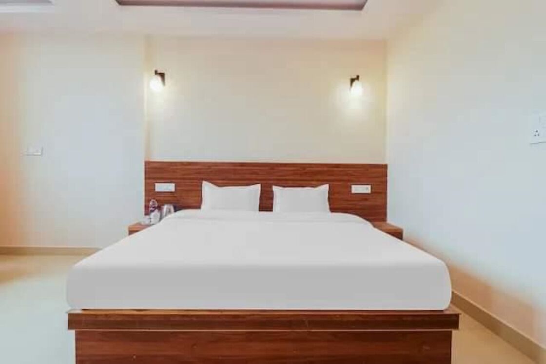 Een netjes opgemaakt bed in een hotelkamer, met een houten hoofdeinde en twee wandlampen.