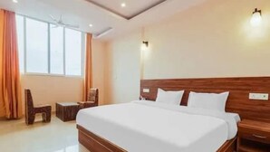 A hotel room with a large bed, wooden headboard, two bedside tables, a chair, and a window with curtains. - Rabbit Hut Guest House By GRB (Dehradun)