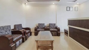 A modern living room with a glass-top coffee table, dark brown sofas, and a wooden sideboard. - Rabbit Hut Guest House By GRB (Dehradun)