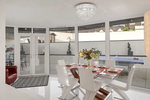 A modern dining area with a glass table, white chairs, and a chandelier.
