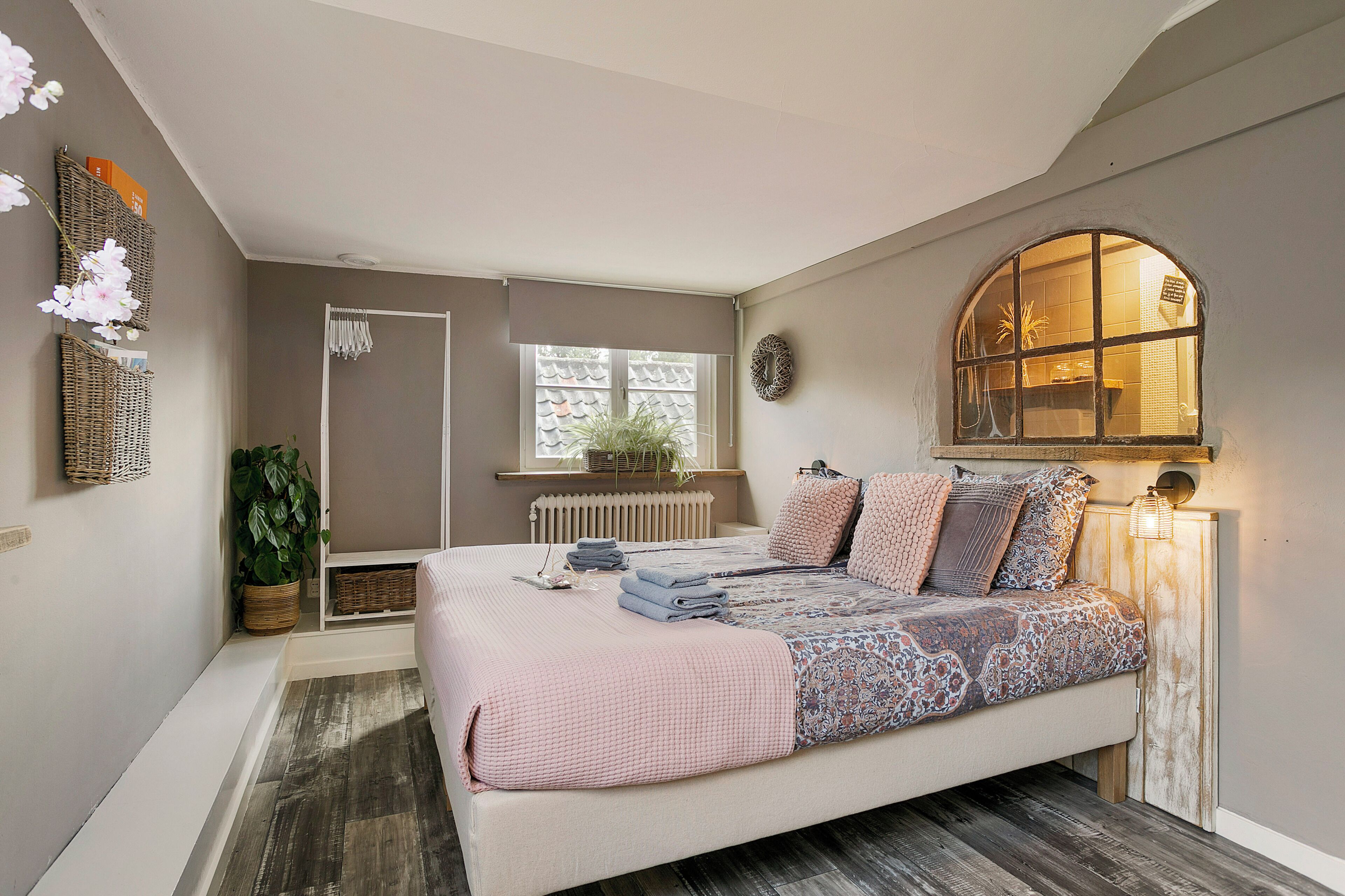 Un dormitorio con una cama grande, una ventana con vistas, un radiador y una planta en maceta.