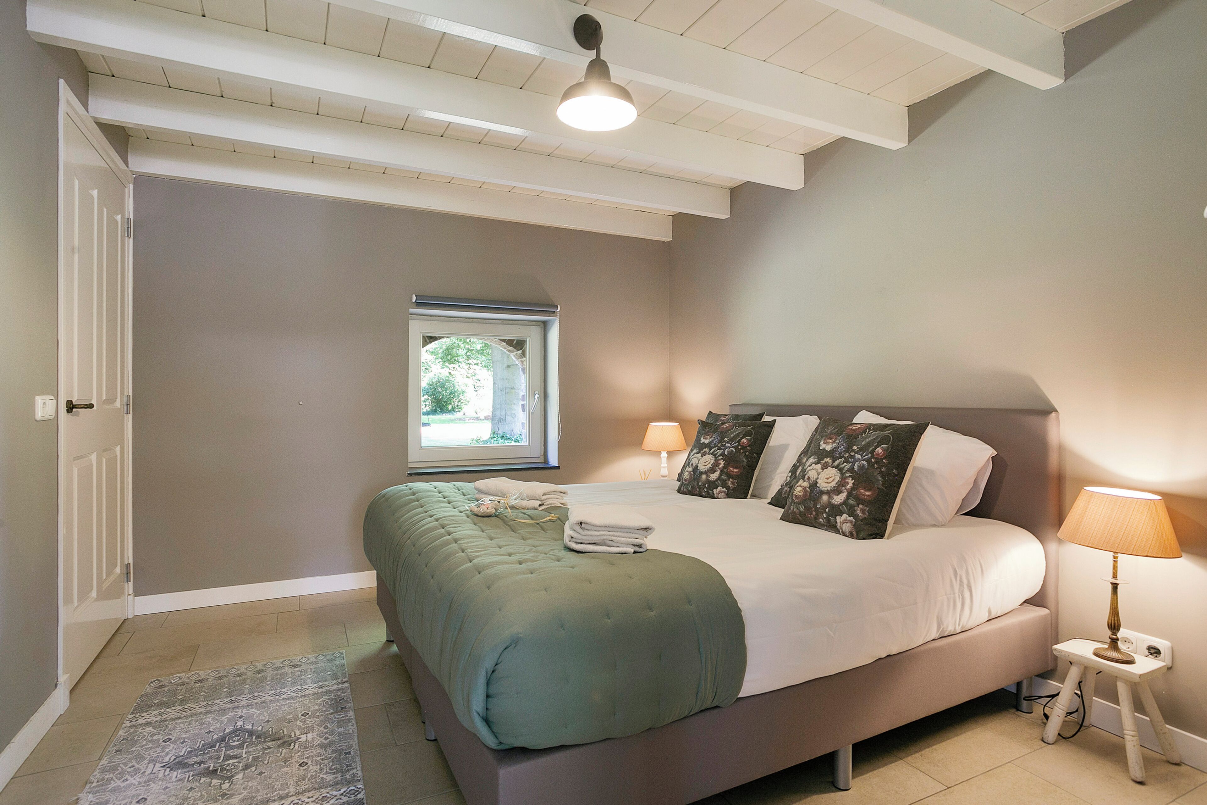 A bedroom with a bed, bedside lamps, a window, and a door.