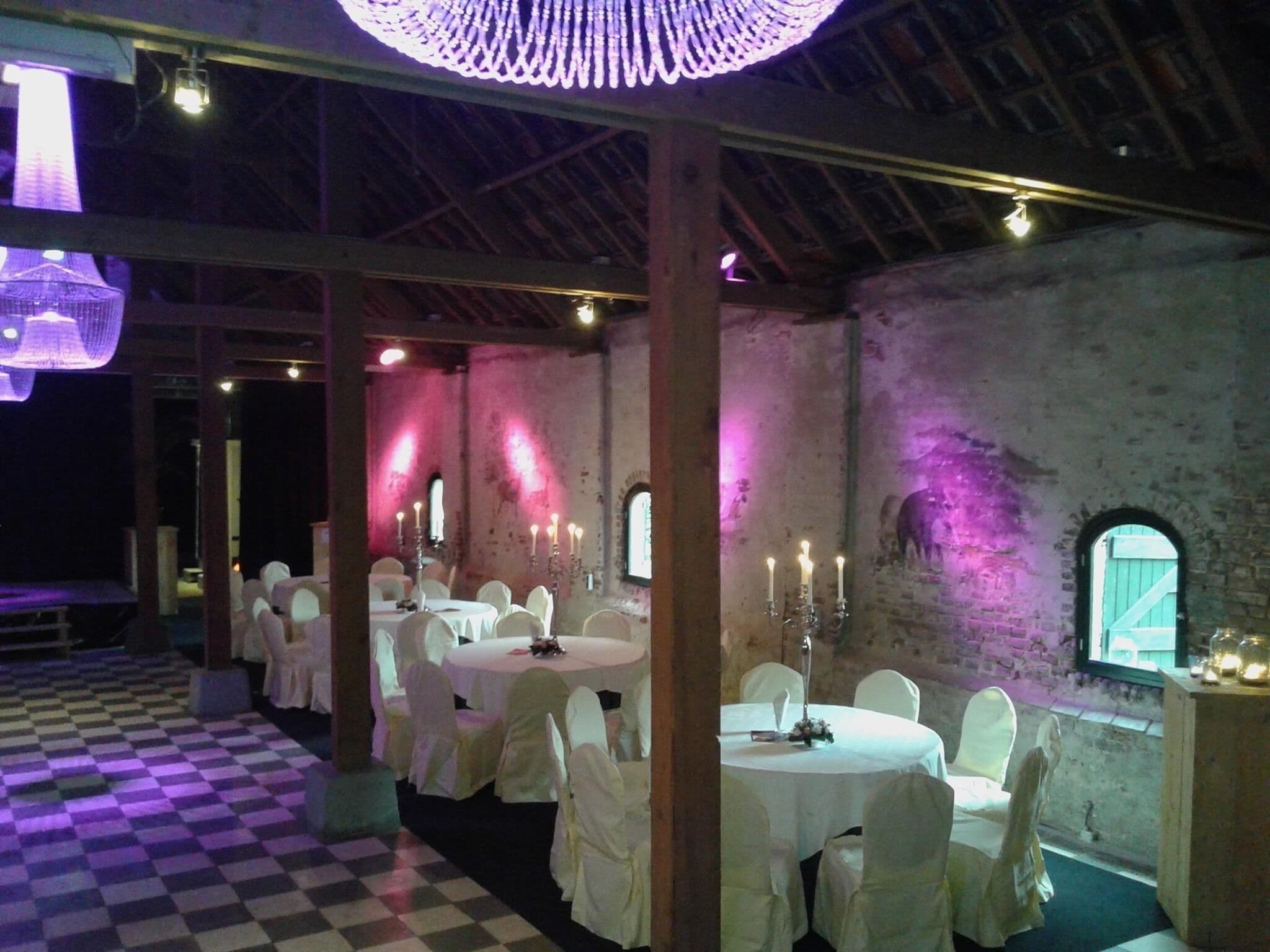 A banquet hall with round tables and chairs, a checkered floor, and a rustic brick wall.