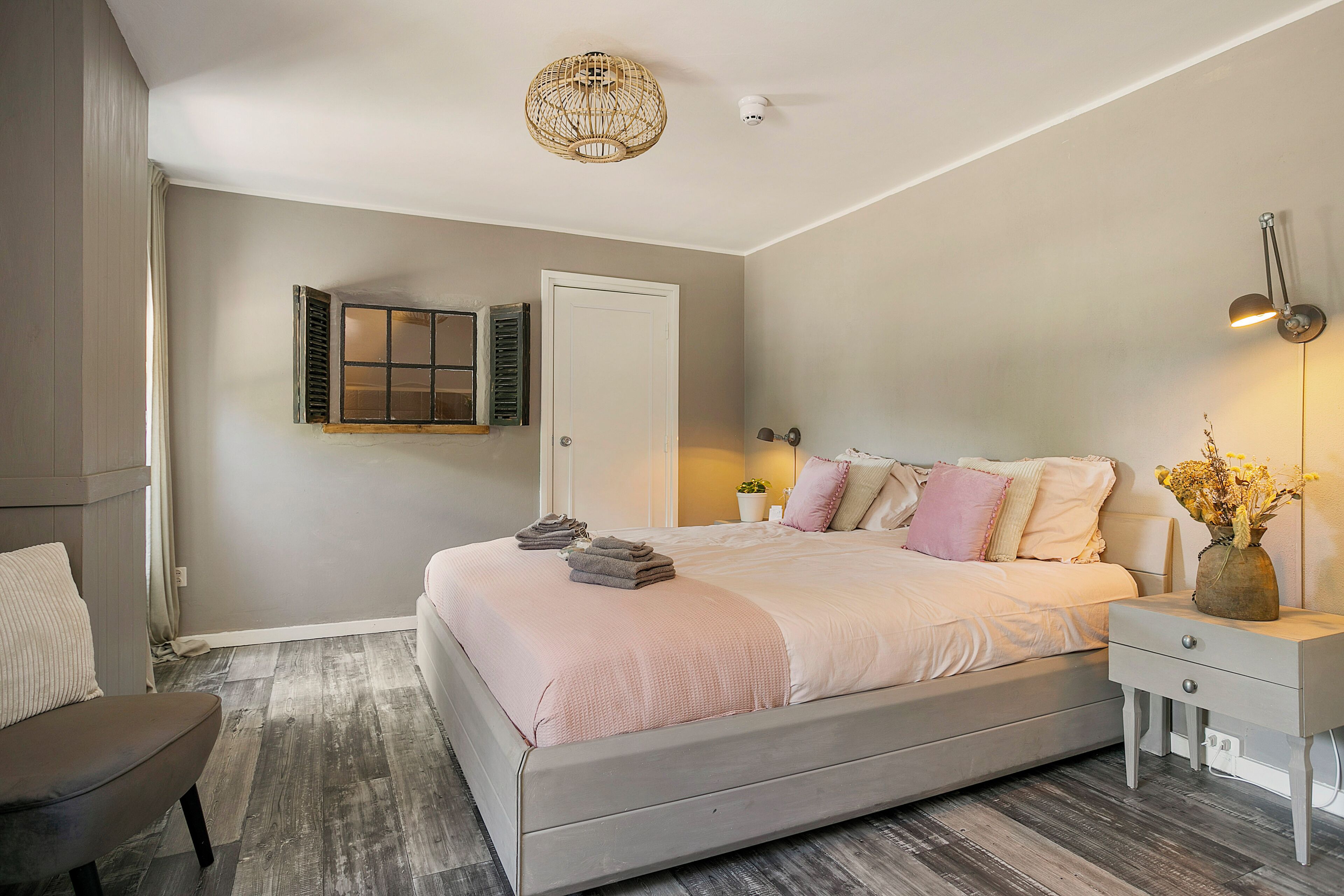 A bedroom with a bed, bedside tables, a chair, a door, and a ceiling light fixture.