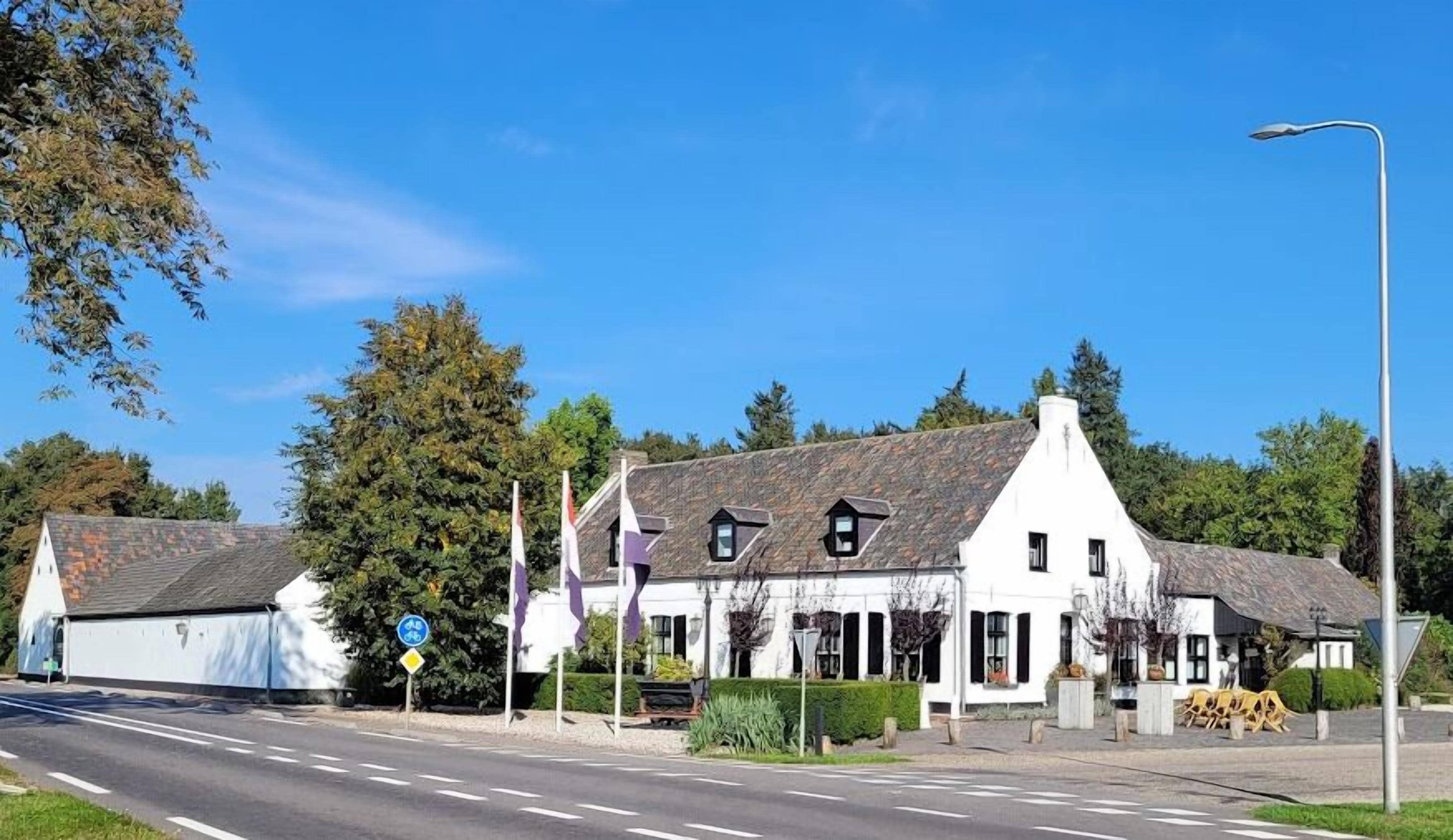 A white building with a stone roof, a bike lane sign, and a pedestrian crossing.