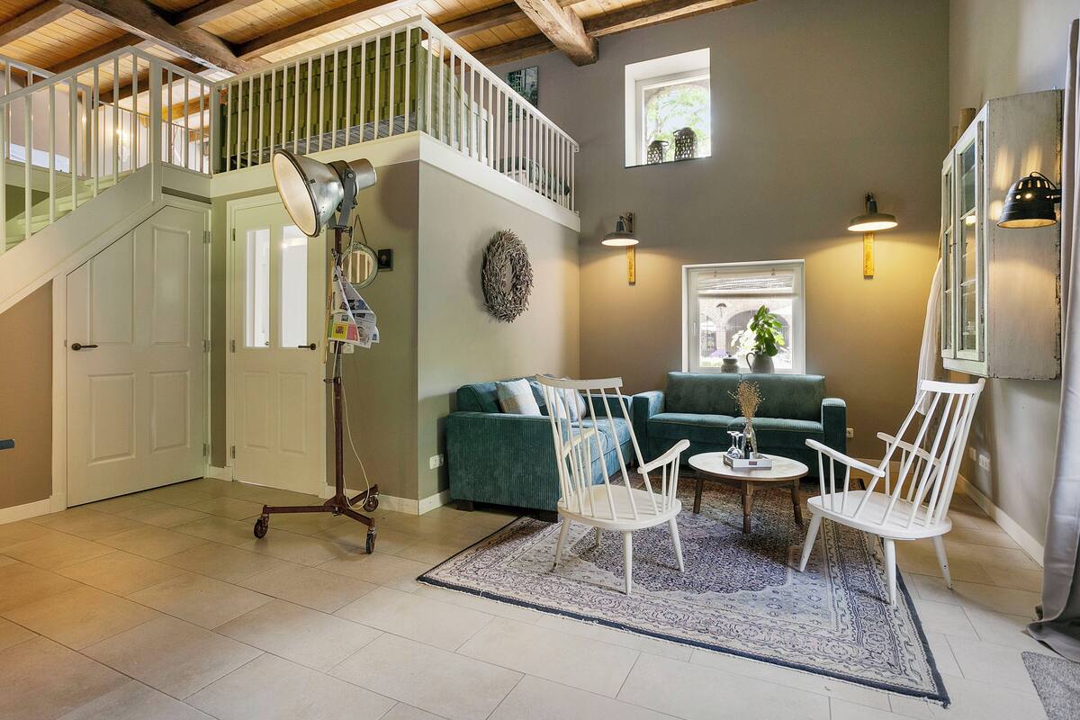 Un vaste espace de vie comprenant un escalier, un canapé vert, des chaises blanches et une petite table.