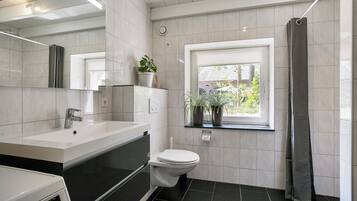 A modern bathroom with a white sink, black countertop, and a toilet. There is a window with a view of greenery outside.