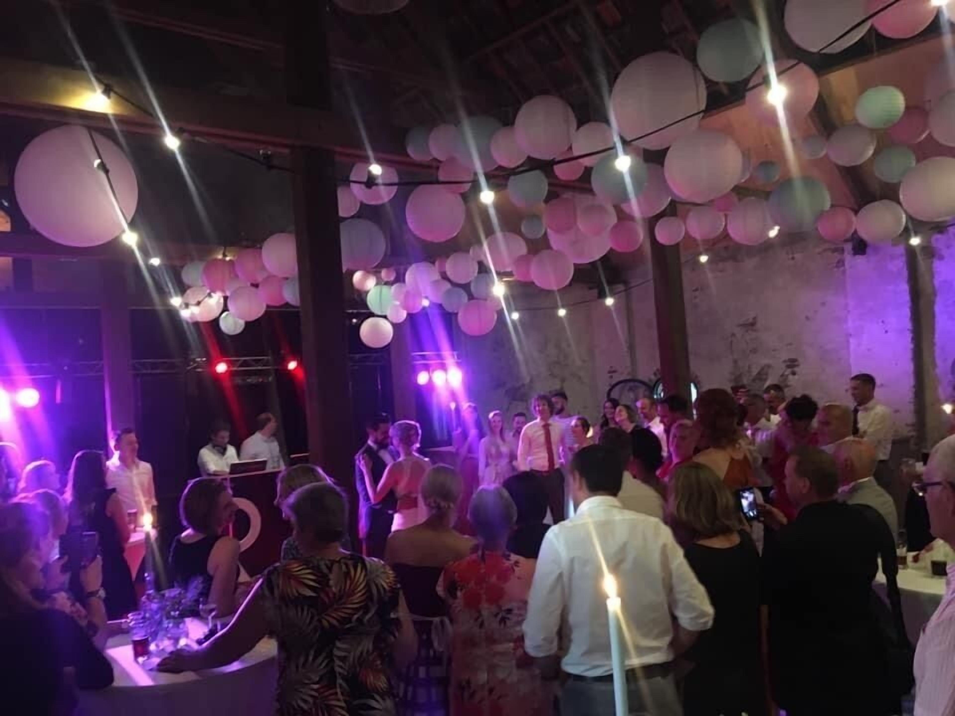 A crowded indoor event with tables and chairs, and people standing and walking around.
