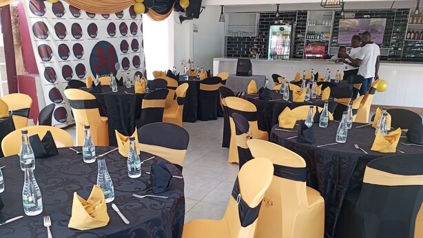 A banquet hall with round tables, black and yellow tablecloths, and chairs with black and yellow sashes. - mirok gardens kisumu (Kisumu)