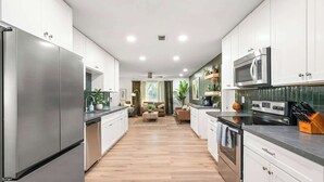 Una cocina moderna con electrodomésticos de acero inoxidable, armarios blancos y piso de madera.