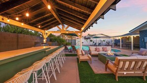 Un patio al aire libre con barra, asientos y piscina.