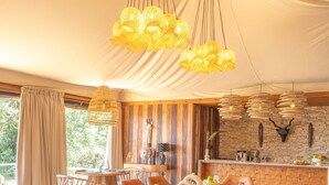 Un vaste espace dédié à la salle à manger, avec une longue table en bois, des chaises en cuir marron et des lampes suspendues jaunes.