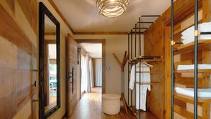 Un intérieur en bois avec un couloir menant à une pièce dotée d’un grand miroir et d’un pouf rond.