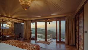 Une chambre spacieuse avec un grand lit, un bureau et une vue sur un paysage montagneux, grâce à de grandes portes coulissantes.