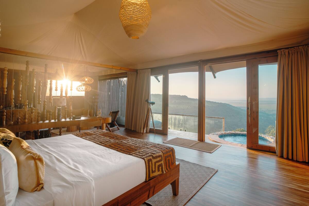 Ein geräumiges Schlafzimmer mit einem großen Bett, einem Holztisch und Blick auf eine Berglandschaft durch große Fenster.