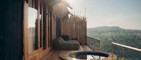 A wooden deck with a hot tub, a sofa, and a view of a forested landscape.